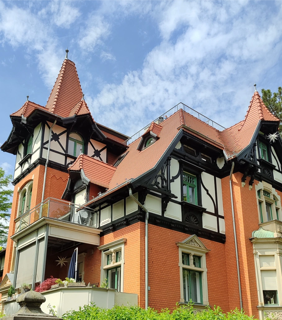Kompleksowy dach zabytkowej willi pokryty czerwonymi dachówkami ceramicznymi i ozdobnymi detalami
